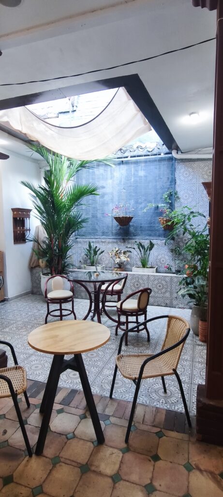 Patio interior con techo de tela, palmeras y mesas en Somos Legados Cali